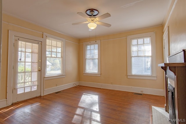 unfurnished living room with ceiling fan, hardwood / wood-style floors, ornamental molding, and a brick fireplace