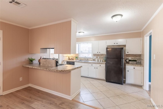 kitchen with black refrigerator, tasteful backsplash, white cabinets, and crown molding