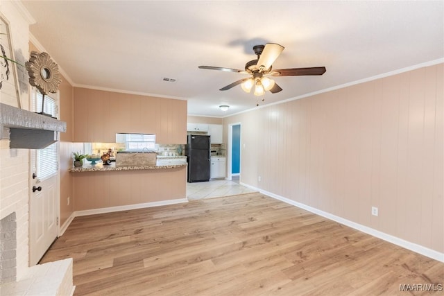 kitchen featuring black refrigerator, kitchen peninsula, a brick fireplace, ornamental molding, and light hardwood / wood-style flooring