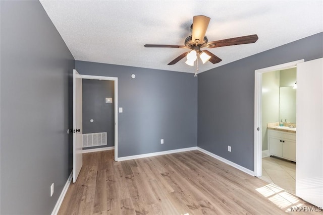 unfurnished bedroom featuring ensuite bath, ceiling fan, sink, light hardwood / wood-style floors, and a textured ceiling