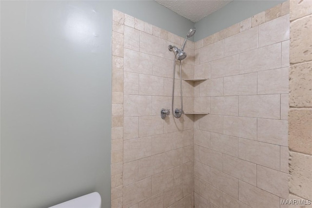 bathroom with a textured ceiling and tiled shower