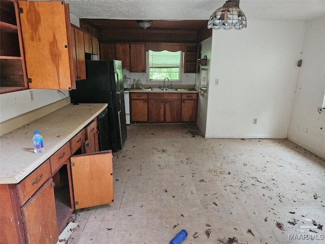 kitchen with a textured ceiling, decorative light fixtures, black fridge, and sink