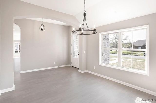 unfurnished dining area with an inviting chandelier, baseboards, dark wood-style floors, and arched walkways