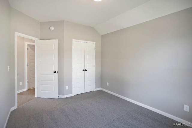 unfurnished bedroom featuring lofted ceiling, a closet, dark colored carpet, and baseboards