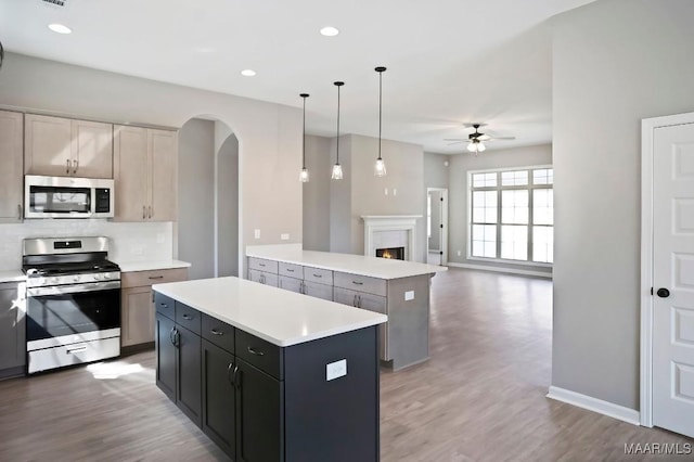 kitchen featuring stainless steel appliances, a center island, a ceiling fan, light countertops, and arched walkways