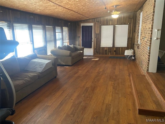 unfurnished living room with brick wall, a textured ceiling, ceiling fan, wooden walls, and hardwood / wood-style flooring