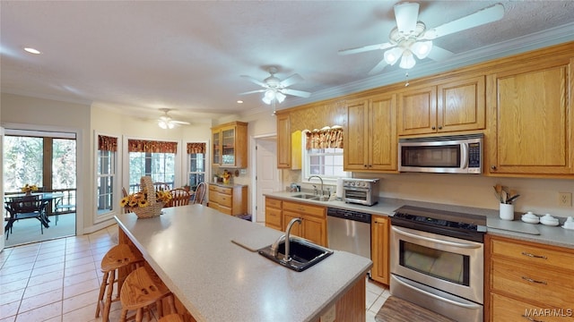 kitchen with a kitchen bar, appliances with stainless steel finishes, ornamental molding, sink, and an island with sink