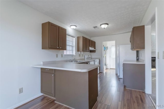 kitchen featuring white electric range, sink, dark hardwood / wood-style flooring, kitchen peninsula, and a textured ceiling