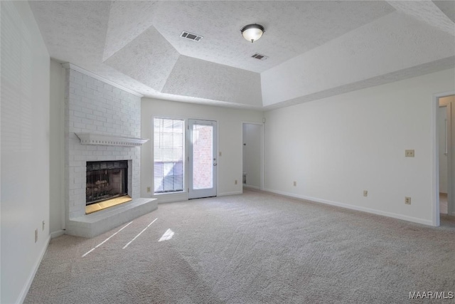 unfurnished living room with light colored carpet, a brick fireplace, a raised ceiling, and a textured ceiling