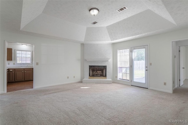 unfurnished living room featuring a raised ceiling, sink, light colored carpet, and a textured ceiling