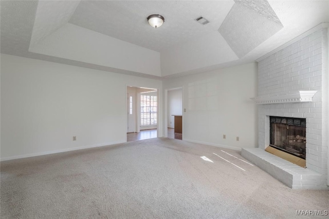 unfurnished living room with a tray ceiling, carpet floors, a brick fireplace, and a textured ceiling