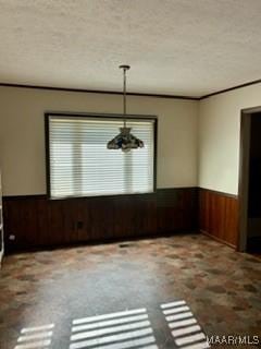 unfurnished dining area featuring a textured ceiling, ornamental molding, and wood walls