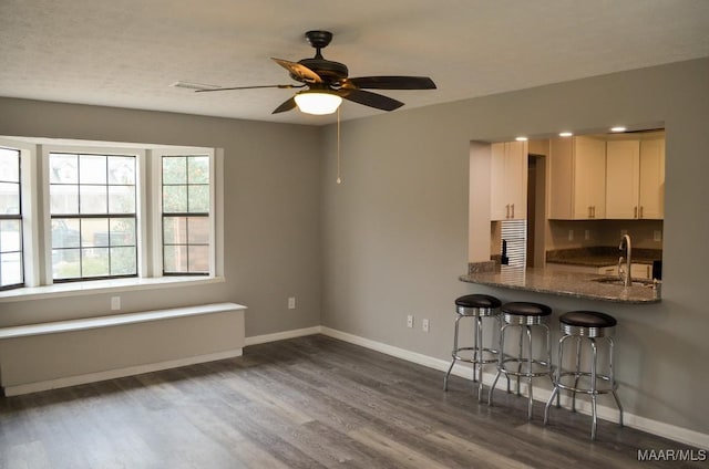 kitchen featuring dark wood-type flooring, dark stone counters, a kitchen breakfast bar, sink, and ceiling fan