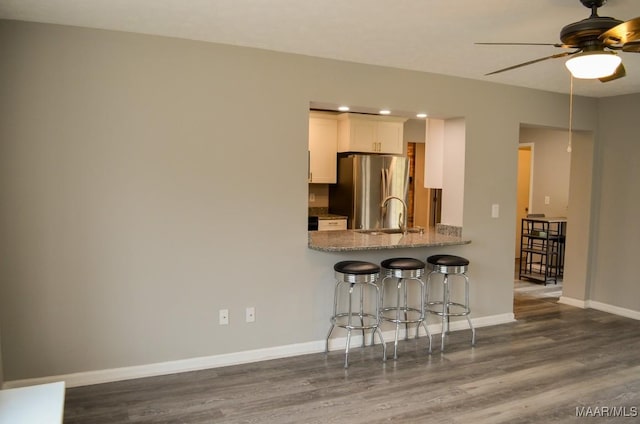 kitchen featuring kitchen peninsula, a breakfast bar, ceiling fan, dark hardwood / wood-style floors, and white cabinetry