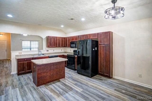 kitchen featuring lofted ceiling, black appliances, light wood-type flooring, decorative light fixtures, and a kitchen island