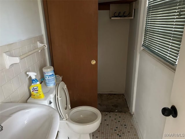 bathroom with toilet, tile patterned flooring, tile walls, and sink