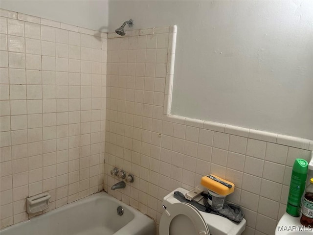 bathroom with tiled shower / bath combo, toilet, and tile walls