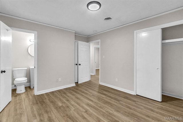 unfurnished bedroom featuring ensuite bathroom, a closet, wood-type flooring, and ornamental molding