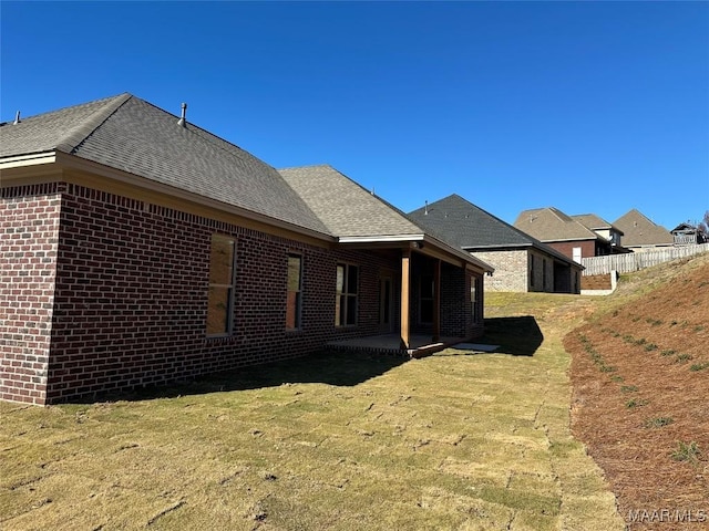 view of property exterior with a yard, a shingled roof, a patio, and brick siding