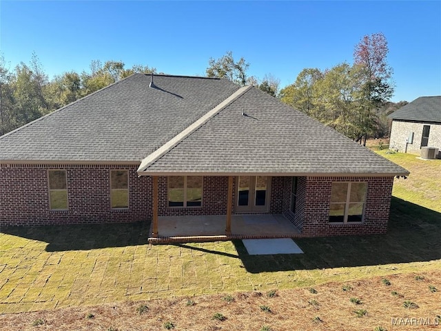 rear view of property with central AC, brick siding, a shingled roof, a lawn, and a patio area