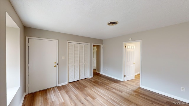 unfurnished bedroom with a textured ceiling, light hardwood / wood-style floors, and two closets