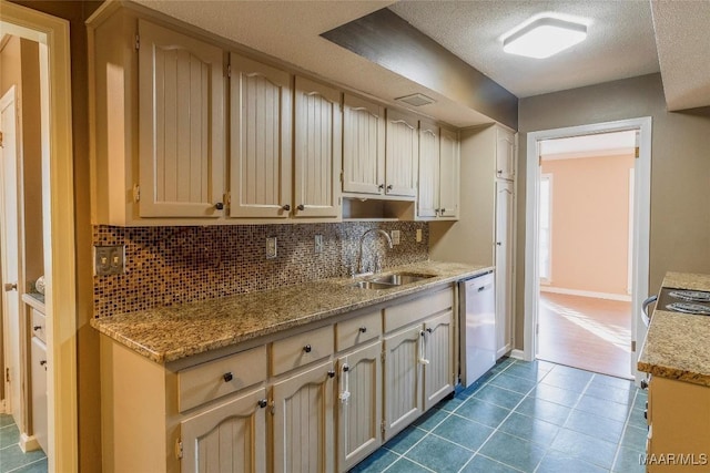 kitchen featuring sink, light stone counters, stainless steel dishwasher, a textured ceiling, and decorative backsplash