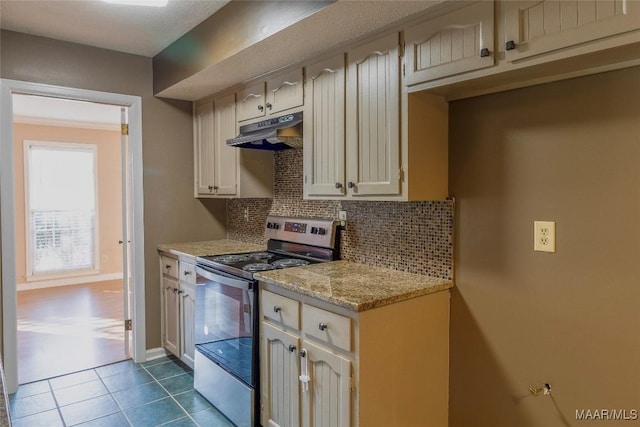 kitchen with light stone countertops, backsplash, cream cabinets, stainless steel range with electric stovetop, and dark tile patterned flooring