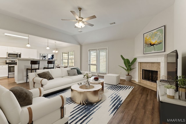 living room with ceiling fan with notable chandelier, dark hardwood / wood-style floors, vaulted ceiling, and a tiled fireplace