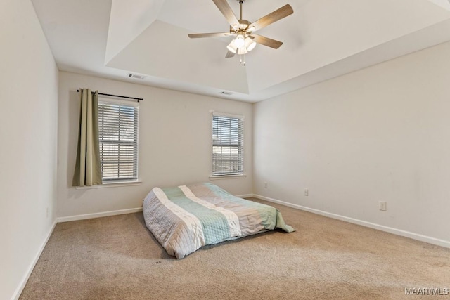 bedroom featuring ceiling fan, light colored carpet, and a tray ceiling