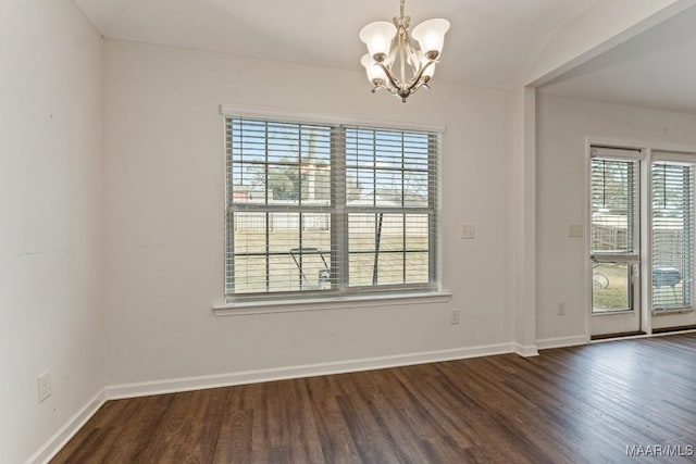 spare room featuring plenty of natural light, dark wood-type flooring, and a chandelier