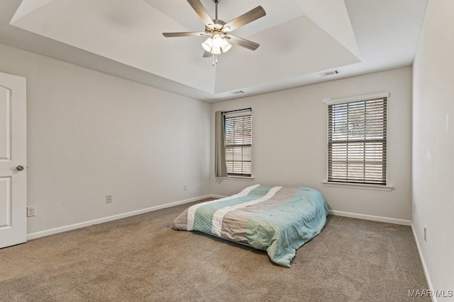 bedroom featuring carpet, a tray ceiling, multiple windows, and ceiling fan