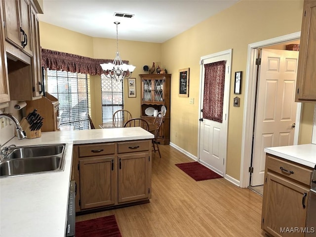 kitchen featuring sink, kitchen peninsula, a chandelier, pendant lighting, and light wood-type flooring