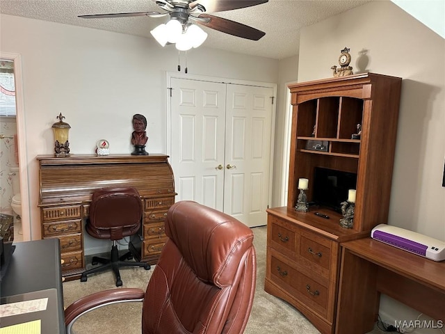 office area with a textured ceiling, light colored carpet, and ceiling fan