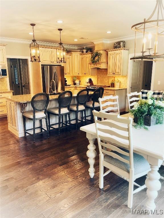 kitchen with stainless steel fridge, a kitchen island with sink, light brown cabinets, pendant lighting, and dark hardwood / wood-style floors