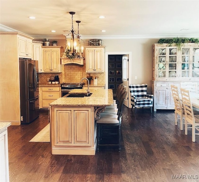 kitchen featuring dark wood-type flooring, sink, refrigerator with ice dispenser, hanging light fixtures, and an island with sink