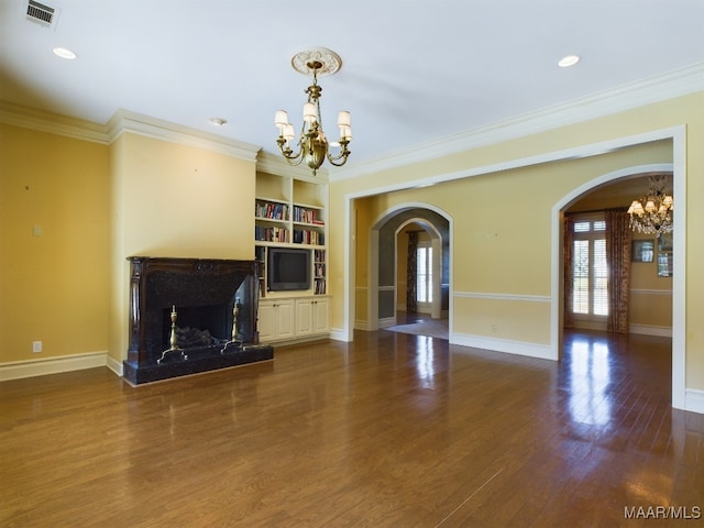 unfurnished living room with built in shelves, a fireplace, crown molding, and a chandelier