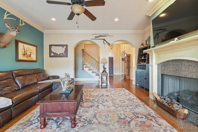 living room with ceiling fan, wood-type flooring, crown molding, and a tiled fireplace