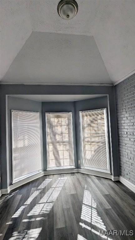 empty room featuring brick wall, dark wood-type flooring, and lofted ceiling