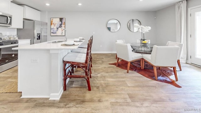 kitchen with sink, stainless steel appliances, a kitchen breakfast bar, a center island with sink, and white cabinets