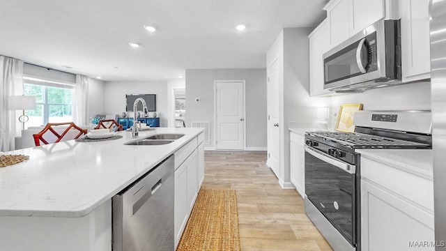 kitchen with appliances with stainless steel finishes, a kitchen island with sink, sink, light hardwood / wood-style flooring, and white cabinets