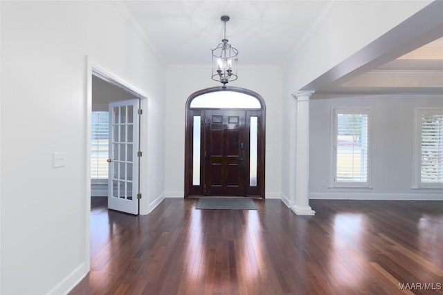 entrance foyer with a notable chandelier, dark hardwood / wood-style flooring, crown molding, and decorative columns