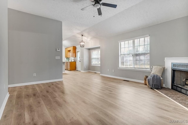 unfurnished living room featuring ceiling fan with notable chandelier, light hardwood / wood-style floors, a textured ceiling, and vaulted ceiling