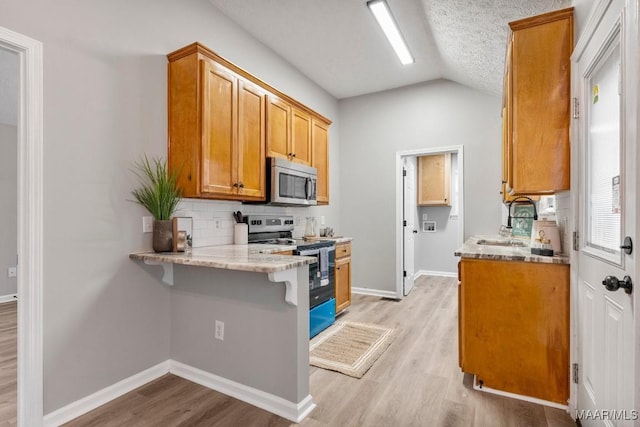 kitchen featuring a breakfast bar, light hardwood / wood-style flooring, lofted ceiling, and appliances with stainless steel finishes