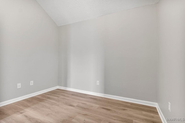 empty room featuring lofted ceiling, a textured ceiling, and light hardwood / wood-style flooring