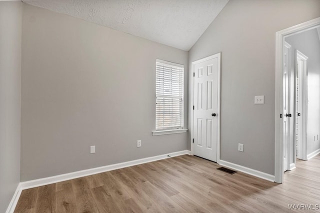 unfurnished bedroom featuring a textured ceiling, vaulted ceiling, and light wood-type flooring