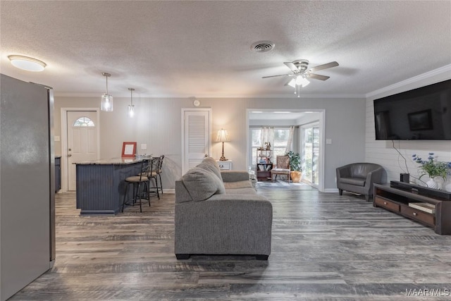 living room featuring crown molding, dark hardwood / wood-style flooring, ceiling fan, and a textured ceiling