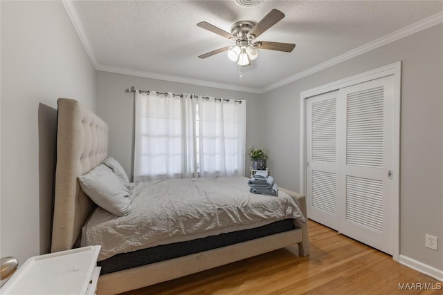 bedroom with crown molding, light hardwood / wood-style flooring, ceiling fan, a textured ceiling, and a closet