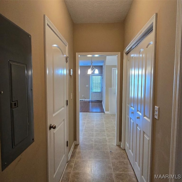 hall with light tile patterned floors, a textured ceiling, and electric panel