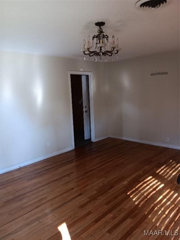 spare room with dark hardwood / wood-style flooring and a chandelier