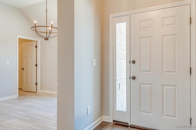 foyer entrance featuring vaulted ceiling, light wood finished floors, baseboards, and an inviting chandelier